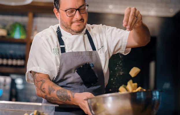 A person in a chef's attire is skillfully tossing food in a bowl, focused on their culinary task, in a kitchen setting.
