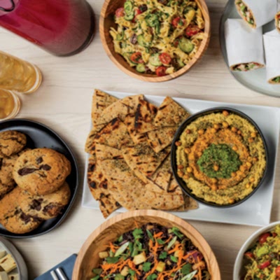 An assortment of Mediterranean-inspired dishes, featuring salad, flatbread with hummus, cookies, and wraps, beautifully arranged on a wooden table.
